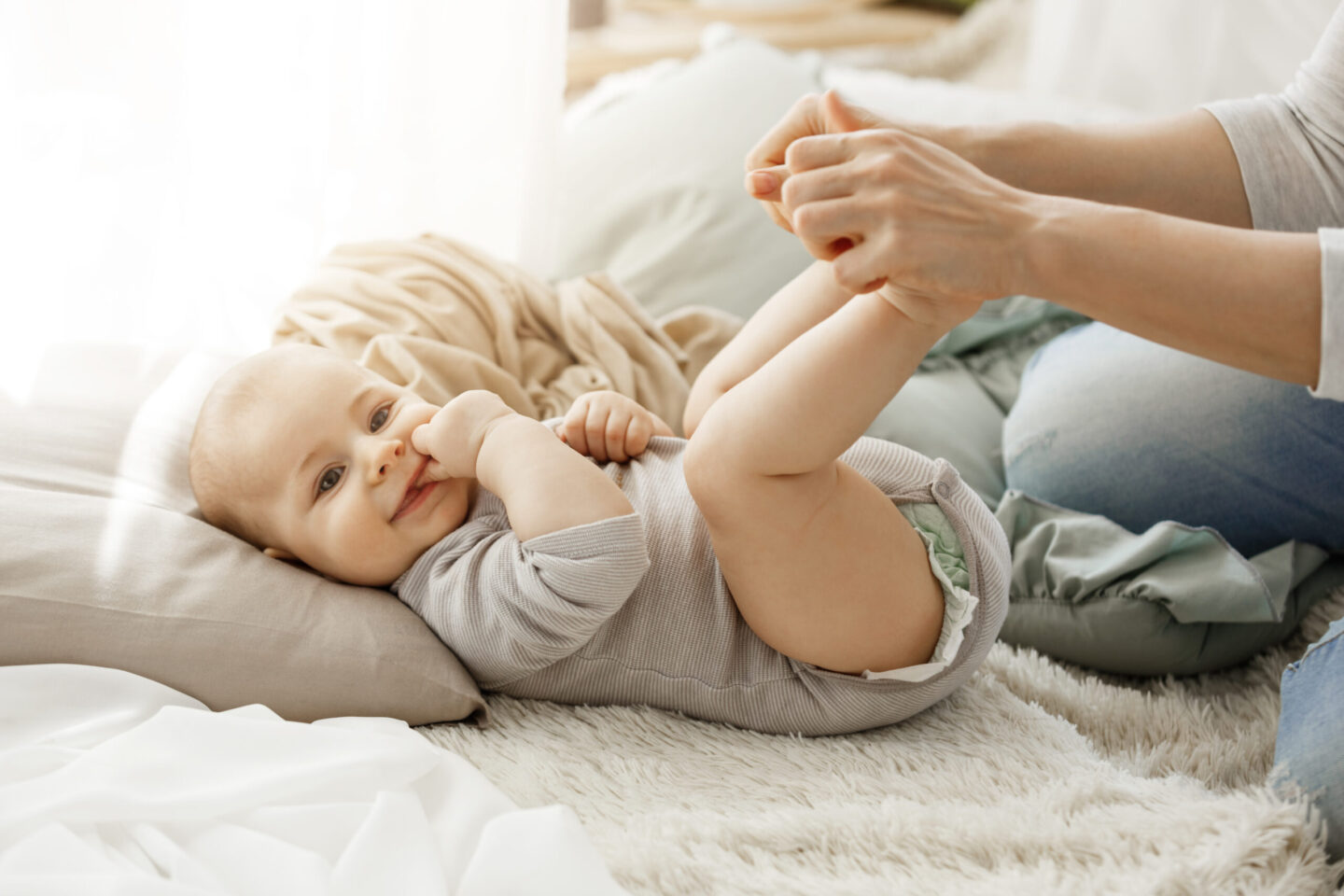 Close up portrait of little newborn son looking at camera while playing with mother. Kid smiling and put his fingers in mouth lookin happy and carefree